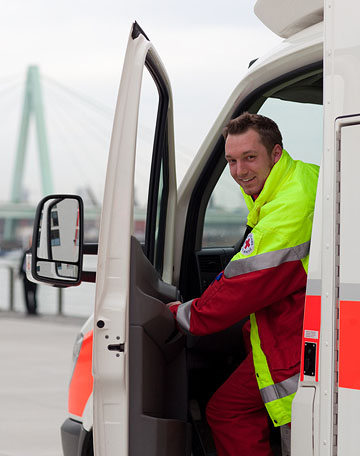 Foto: Ein Rettungssanitäter öffnet lächelnd die Tür eines Rettungswagens.